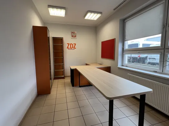 Pokój biurowy z długim biurkiem narożnym, szafami i witryną.