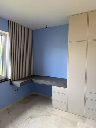 Pokój z narożnym biurkiem, ścianą z lamelami przy oknie i wysoką jasną szafą