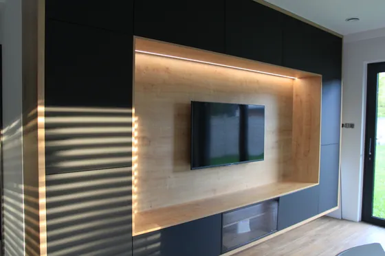 Ciemna ściana RTV z szafkami pod sufit i drewnianą wnęką z podświetleniem LED w salonie.